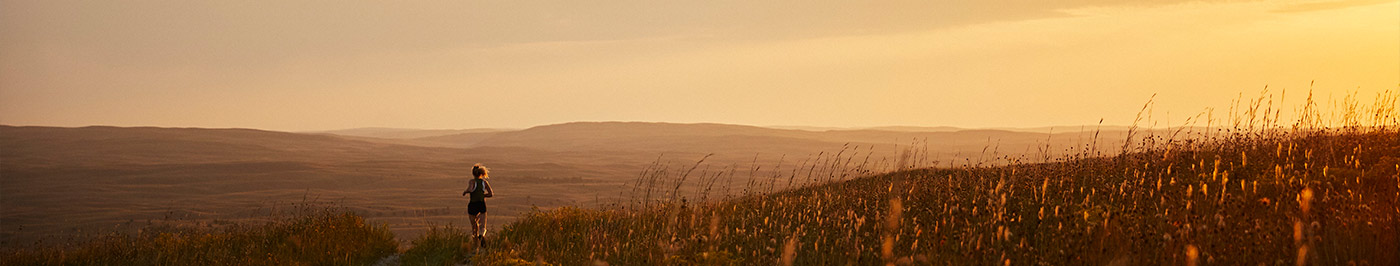 woman running on field trail at sunset